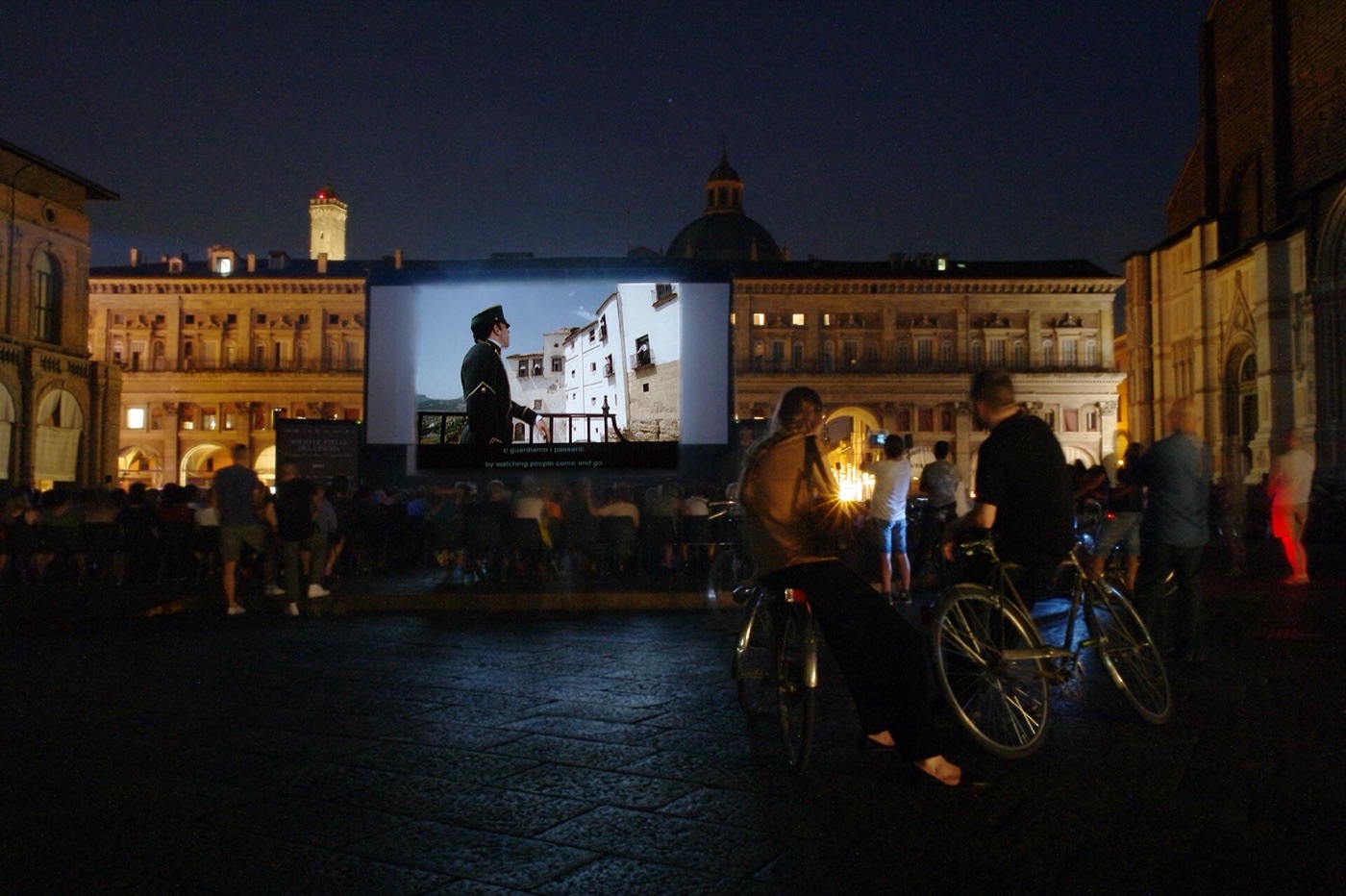 Openluchtbioscoop op Piazza Maggiore in Bologna: een groot doek voor oude gevels, bezoekers met fietsen.