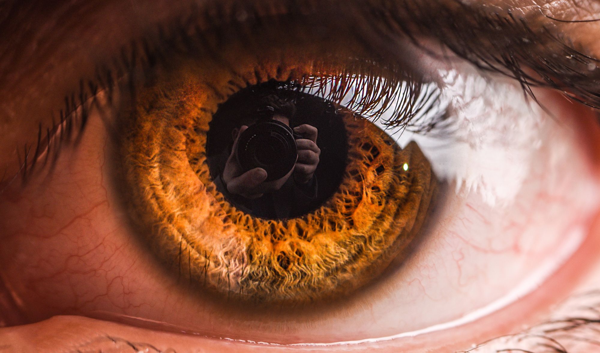 Extreme close-up van een oog; in de pupil is een fotograaf met camera te zien.