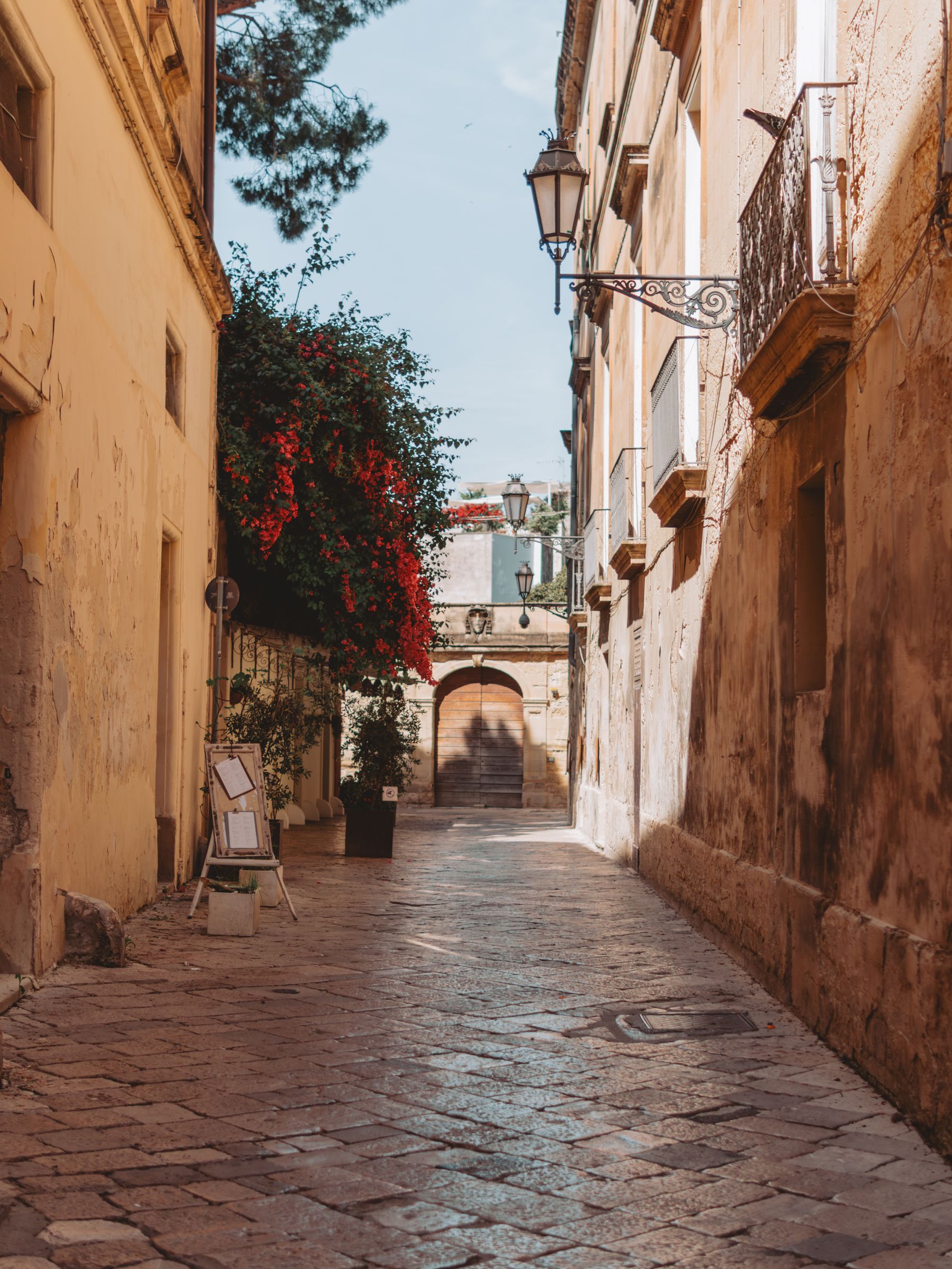 Een smal steegje in Lecce met bloeiende planten tegen lichte stenen gevels.