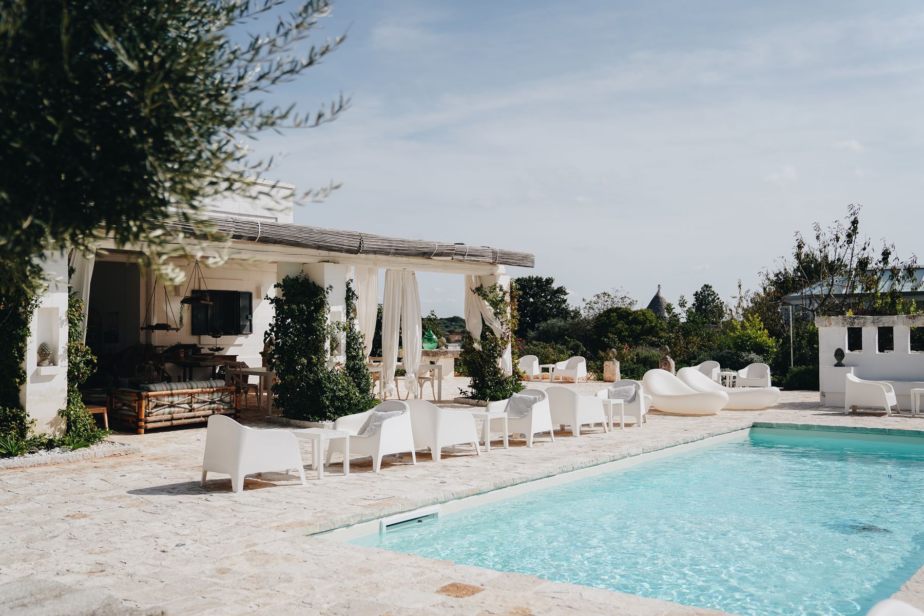 Een witte masseria met een zwembad en een terras met linnen doeken, met een trullo op de achtergrond.